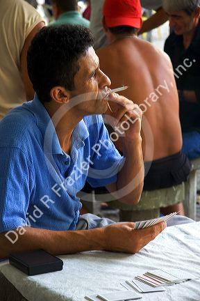 Man smoking a cigarette while playing a game of cards at a park in Rio de Janeiro, Brazil.