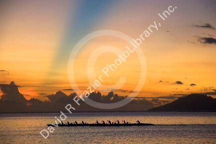 Outrigger canoeing at sunset off the island of Tahiti. The blue band in the sky is believed to be the shadow cast from a mountain on a distant island.