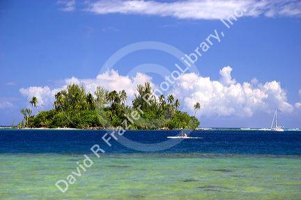 Small island called a Motu, outrigger canoe, and a sailboat off the island of Moorea.
