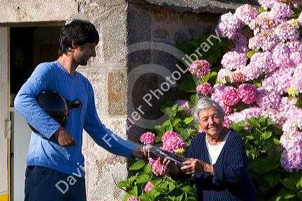 French letter carrier delivering mail to an elderly woman in the commune of Barfleur in the region of Basse-Normandie, France.