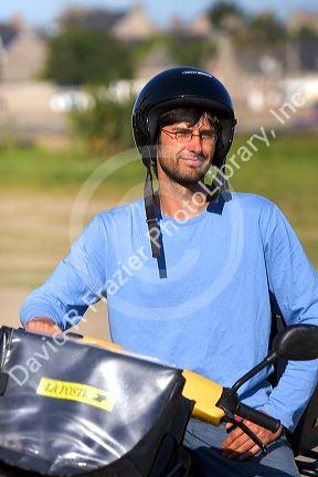 French letter carrier on a scooter in the commune of Barfleur in the region of Basse-Normandie, France.
