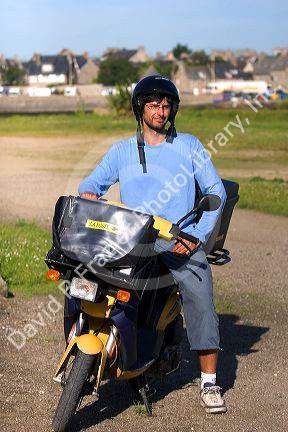 French letter carrier on a scooter in the commune of Barfleur in the region of Basse-Normandie, France.