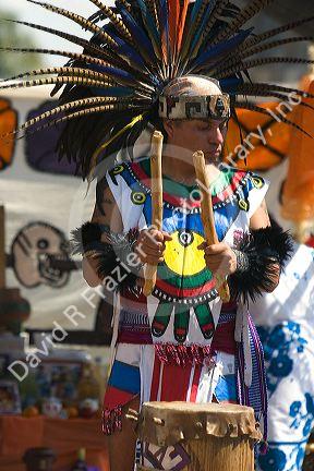 Aztec indian man wearing a head dress made of pheasant feathers playing the drum during a celebration for the Day of the Dead in Mexico City, Mexico.