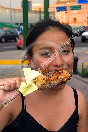 Mexican girl eating an ear of roasted corn on the cob in Mexico City, Mexico.