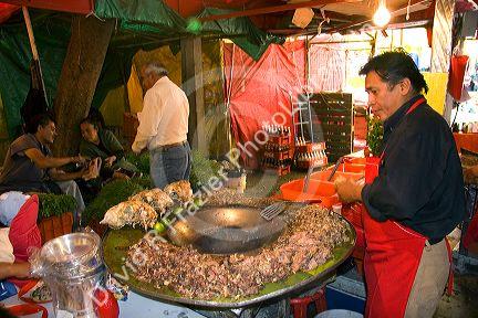 Vendor cooking cabeza tacos using a cazo at the Merced Market in Mexico City, Mexico.