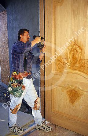 Carpenter using a cordless drill to install a door.