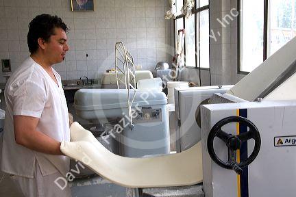 Baker using a machine to roll out dough at the Panaderia Union in Tolhuin, Tierra del Fuego, Argentina.
