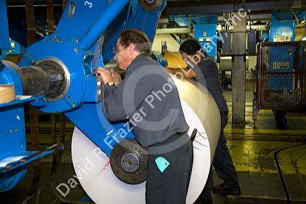 Pressmen loading a large roll of paper onto a rotary printing press for the Houston Chronicle in Houston, Texas.