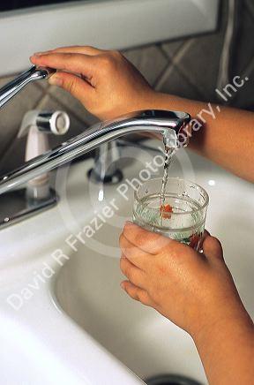 A child getting a glass of water from the kitchen faucet.