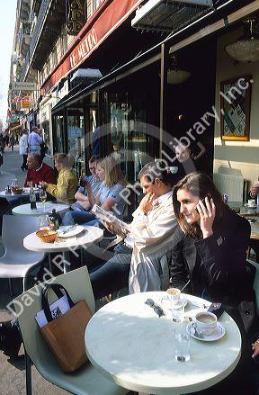 A women using a cell phone at a sidewalk cafe in Paris, France.