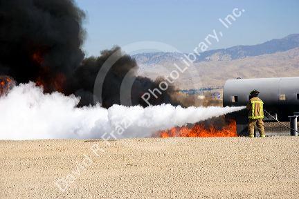 Firefighter using fire retardant foam to put out a jet fuel fire at an airport training facility in Boise, Idaho, USA.