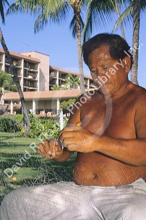 A Hawaiian fisherman repairs a fishing net in Hawaii.
