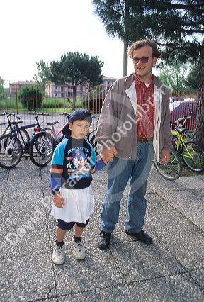 Italian father and son holding hands enroute to school.  The white apron is part of the elementary school uniform.