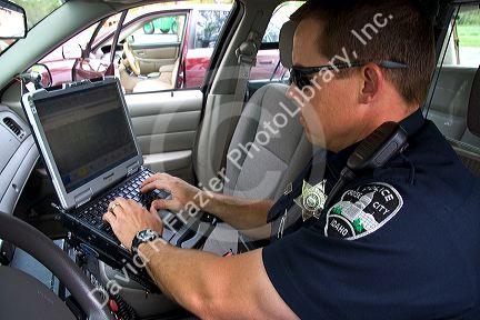 Police officer using a mobile data terminal computer inside a police car in Boise, Idaho, USA.