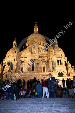 People gather on the steps of the Sacre-Coeur Basilica at night in Paris, France.