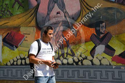 Mexican college student walking in front of a mural on the campus of Universidad Autonoma de Guerro located in Acapulco, Guerrero, Mexico.