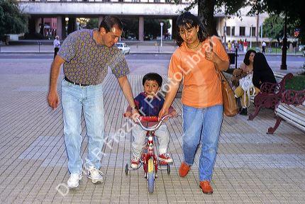 Parents helping child ride a tricycle in Santiago, Chile.