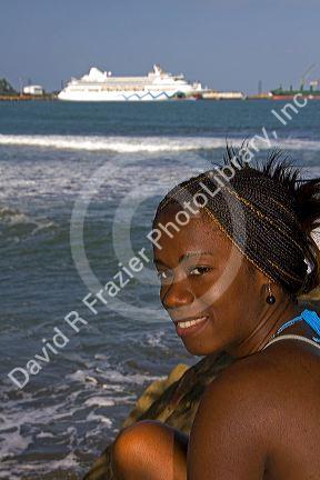 Costa Rican afro-caribbean woman on the beach with the  AIDAaura cruise ship docked in the background at Puerto Limon, Costa Rica.