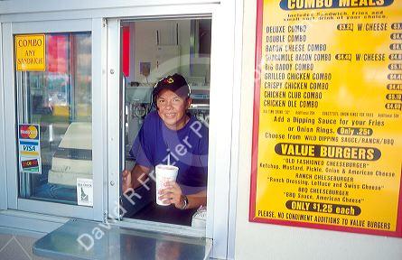 Young woman emplyee of a fast food restaurant serves a milkshake through the drive up window.