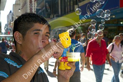 Argentine man blowing bubbles with a Bart Simpson toy along the pedestrian section of Florida Street in the Retiro barrio of Buenos Aires, Argentina.