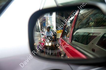 Motorbikes squeezing through car traffic seen through a rear view mirror in Bangkok, Thailand.