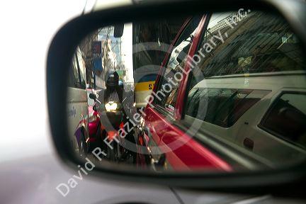 Motorbikes squeezing through car traffic seen through a rear view mirror in Bangkok, Thailand.