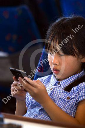 Asian girl playing with a smart phone while on a tour boat in the Bay of Islands, North Island, New Zealand.