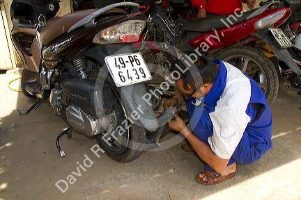 Sidewalk mechanic fixing a flat tire on a scooter in Da Lat, Vietnam.