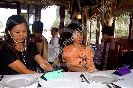 Vietnamese women watching a personal electronic device while on a tour boat in Ha Long Bay, Vietnam.