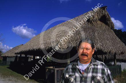 Ted Billie, a seminole Miccosukee Indian standing in front of a chopekcheke traditional thatched roof dwelling in Florida. (model released)