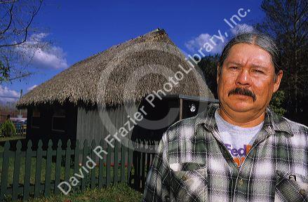 Ted Billie, a seminole Miccosukee Indian, standing in front of a chopekcheke traditional thatched roof dwelling in Florida. (model released)
