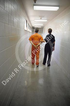 A handcuffed male inmate being escorted down a hall way by a jail guard.