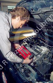 A male adult auto mechanic using a computer on a car engine to figure out what is wrong with it.