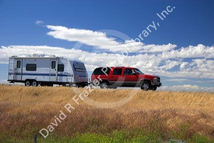 A suburban pulling a camper trailer on the highway.