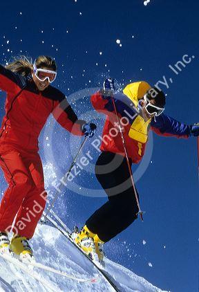 A couple snow skiing with sun glasses and nylon waterproof clothing.