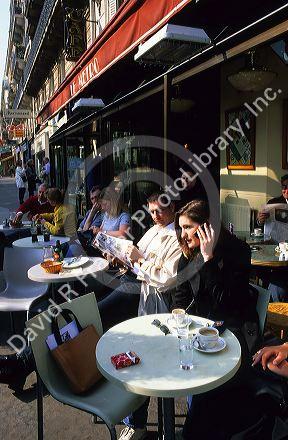 A woman speaks on her cell phone while having coffee at an outdoor cafe in Paris, France.