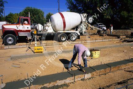 Worker smoothing freshly poured concrete footings, Idaho.