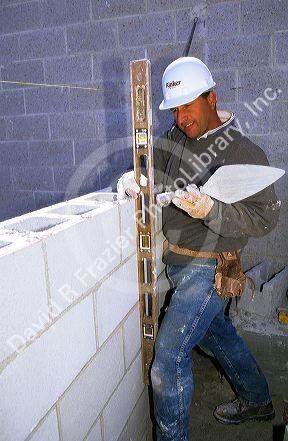 A mason uses a mason line and level to line up course with cinder block wall.