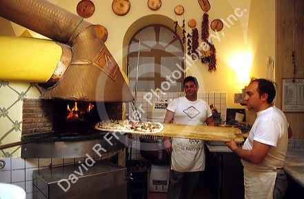 An Italian chef placing a pizza in a wood heated oven, Italy.