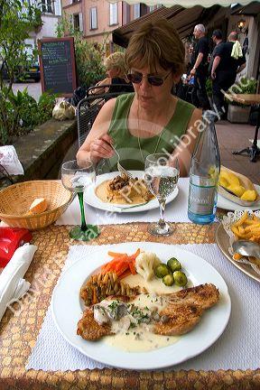Woman dining at sidewalk restaurant in Ribeauville, France.