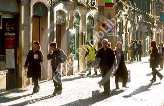 Late afternoon sun highlights pedestrians along Via Della Croce in Rome, Italy.