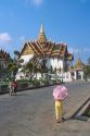 Woman walking with an umbrella in front of the Grand Palace in Thailand.
