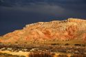 Butte along US highway 550 near Bernalillo, New Mexico with dark storm cloud backdrop in the evening sun.