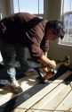 Construction worker installing wood flooring with a flooring nail tool.