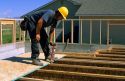Construction worker installing the sub-floor for a new home applies a wood adhesive to prevent the floor from squeaking.