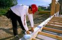 Construction worker installing a foam strip between the wood base plate and the foundation.