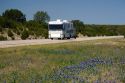 A motorhome recreational vehicle pulling a trailer on Interstate 10 in west Texas with Texas blue bonnet wildflowers in the median.