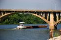 Tug boat and river barge pass under a bridge over the Arkansas River in Little Rock, Arkansas.