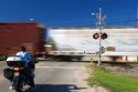 A train in motion passes through a railroad crossing while a motocyclist waits to cross in Iowa.