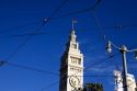 Clock tower on the Ferry Building in San Francisco, California seen through the wires powering trolley cars.